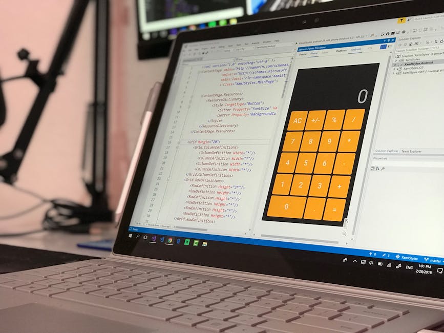 A close-up view of a laptop computer with a silver keyboard, displaying a software development environment on the screen. The code editor shows lines of HTML and CSS code, with syntax highlighting in 